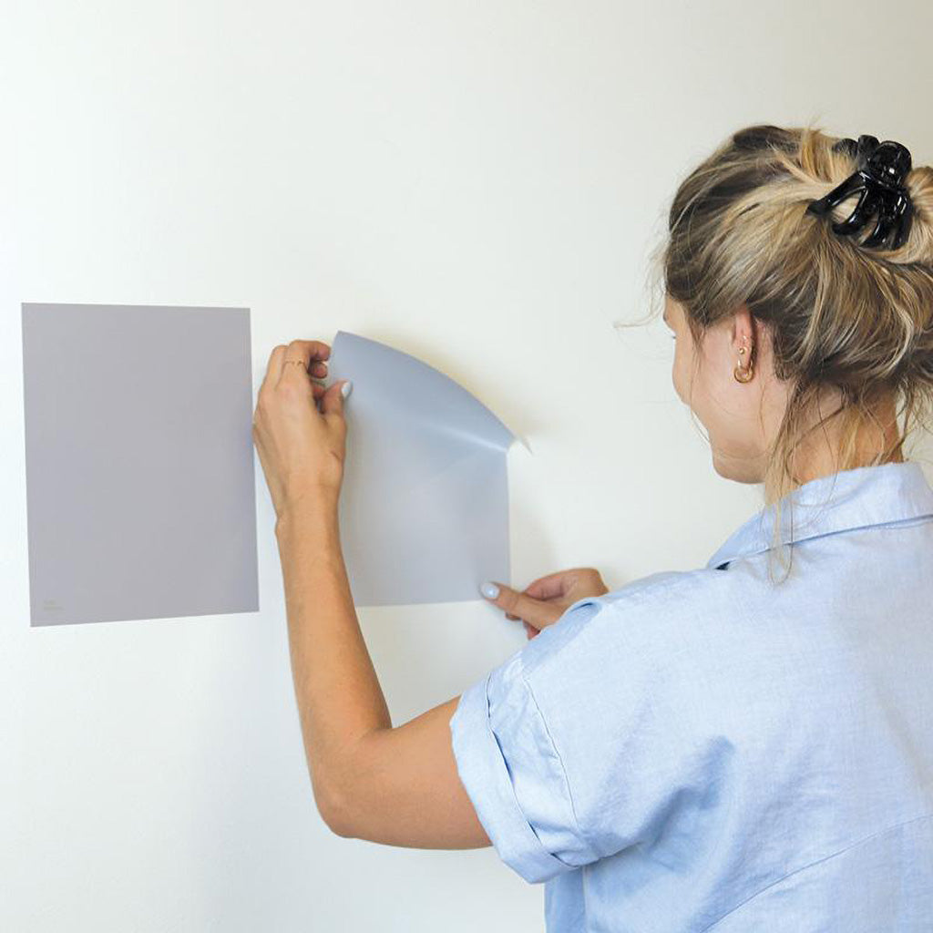 Woman testing peel and stick Room & Board adhesive paint samples on a wall. 