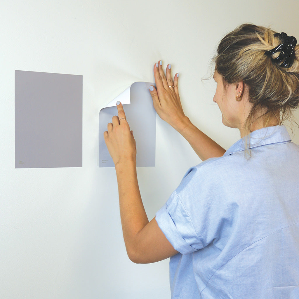 Woman testing peel and stick Room &amp; Board adhesive paint samples on a wall. 