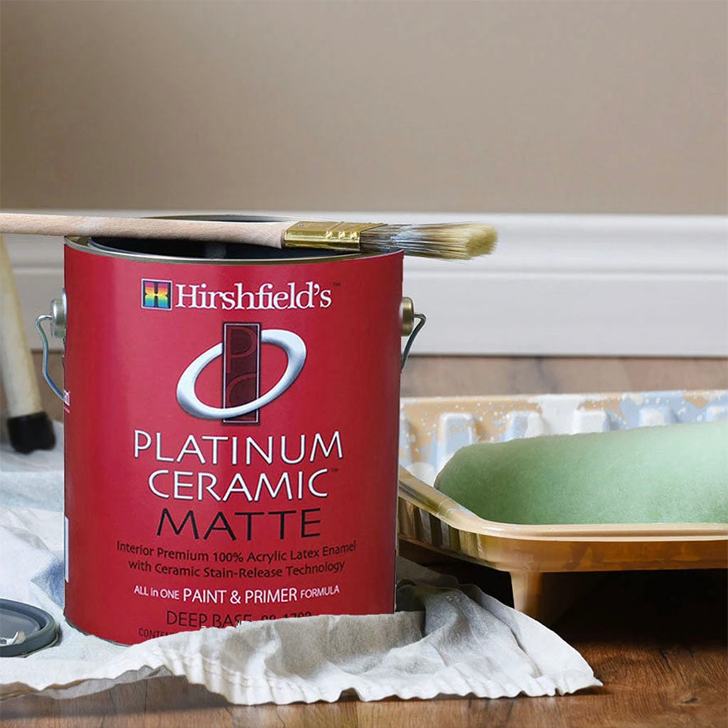 Gallon of Hirshfield's platinum ceramic paint with a paint brush, next to a paint tray and paint roller