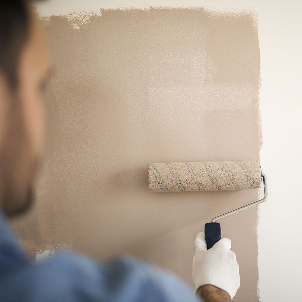 male painting a interior house wall with a paint roller a trendy warm beige/gray paint color